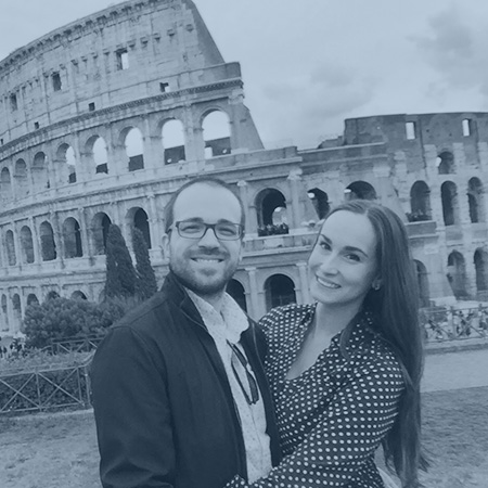 A photograph of Brett Heinz and his partner in front of the Colosseum in Rome, overlaid with a blue filter